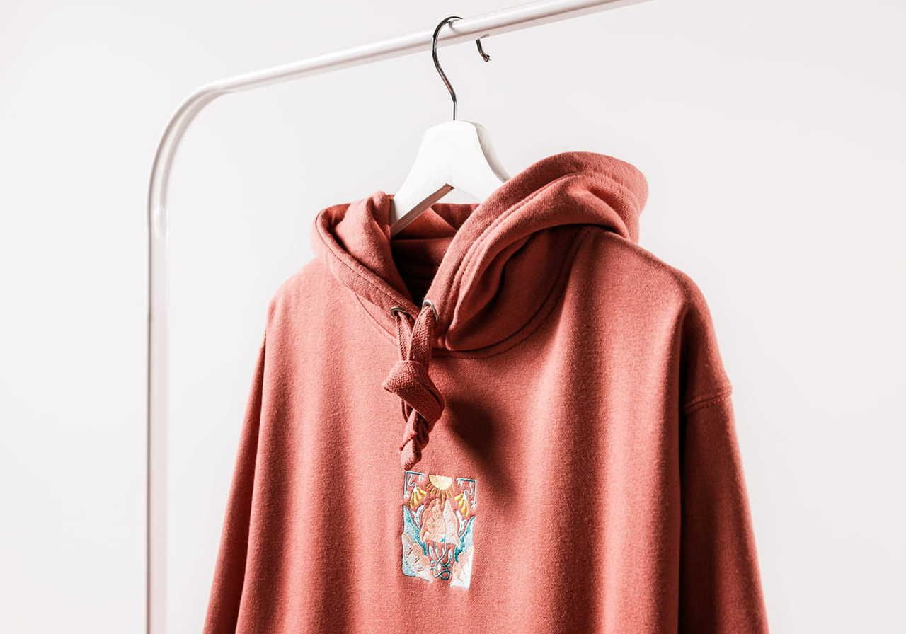 A brown hoodie with am emboridered graphic design hanging on a clothing rack.