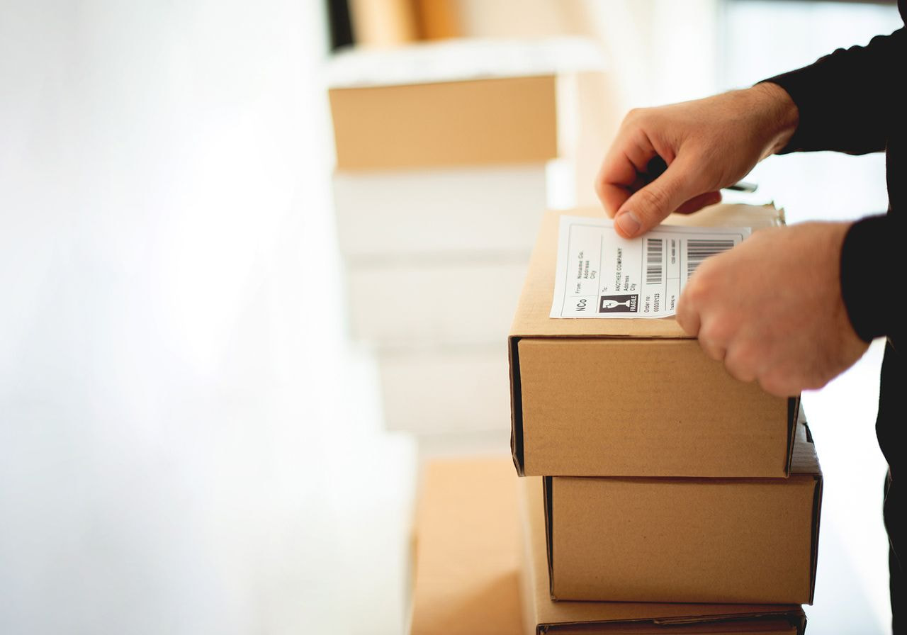 A person attaches a shipping label to a stack of cardboard boxes ready for delivery.