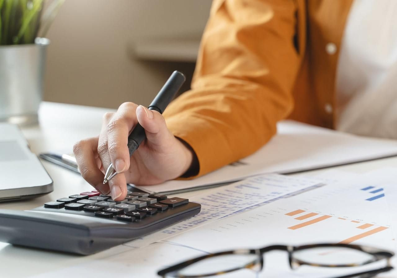 A woman's hand is writing numbers on a calculator, focusing on calculations with a pen in her fingers.
