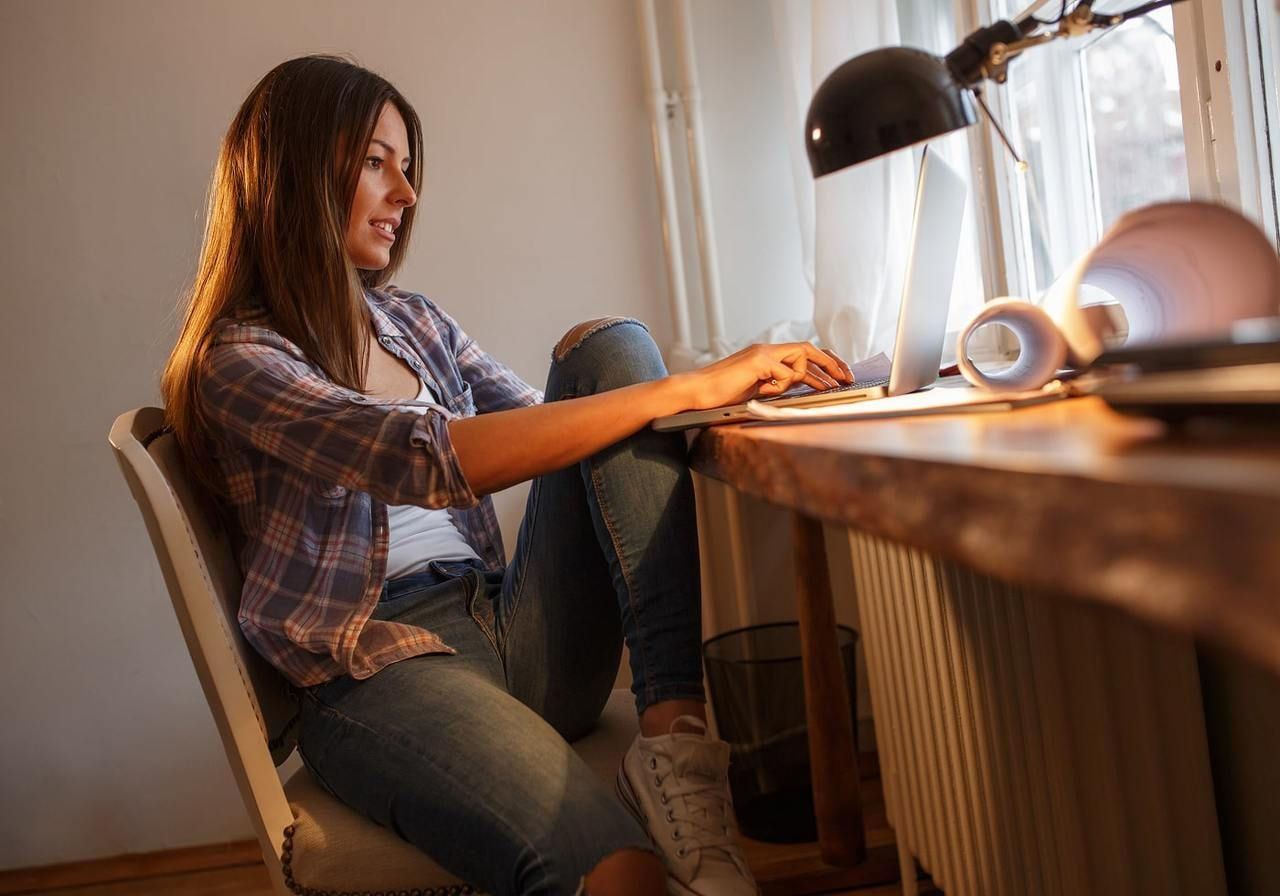 A woman is sitting at a table and using a laptop to start a print-on-demand business. 