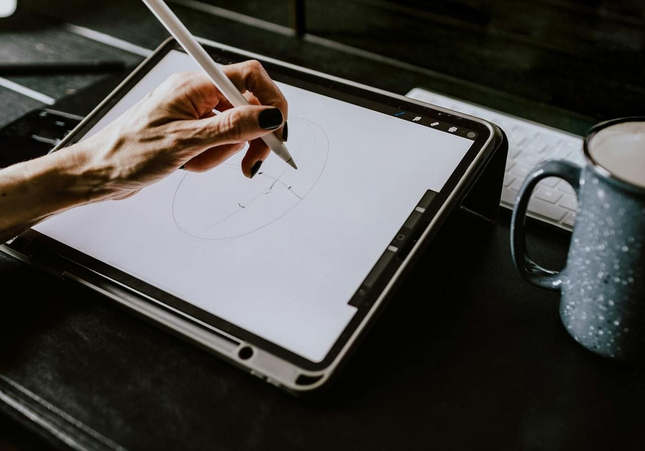 A woman's hand holds a pen, drawing on a digital tablet with a focused expression.