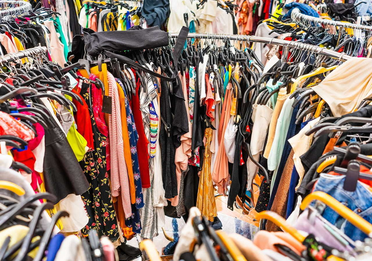 A colorful assortment of clothes is densely packed on round racks in a thrift store.
