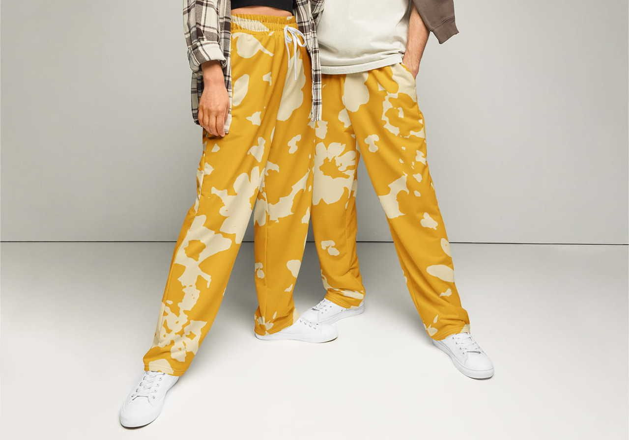 Two people stand with legs apart, wearing yellow sweatpants with white abstract patterns.