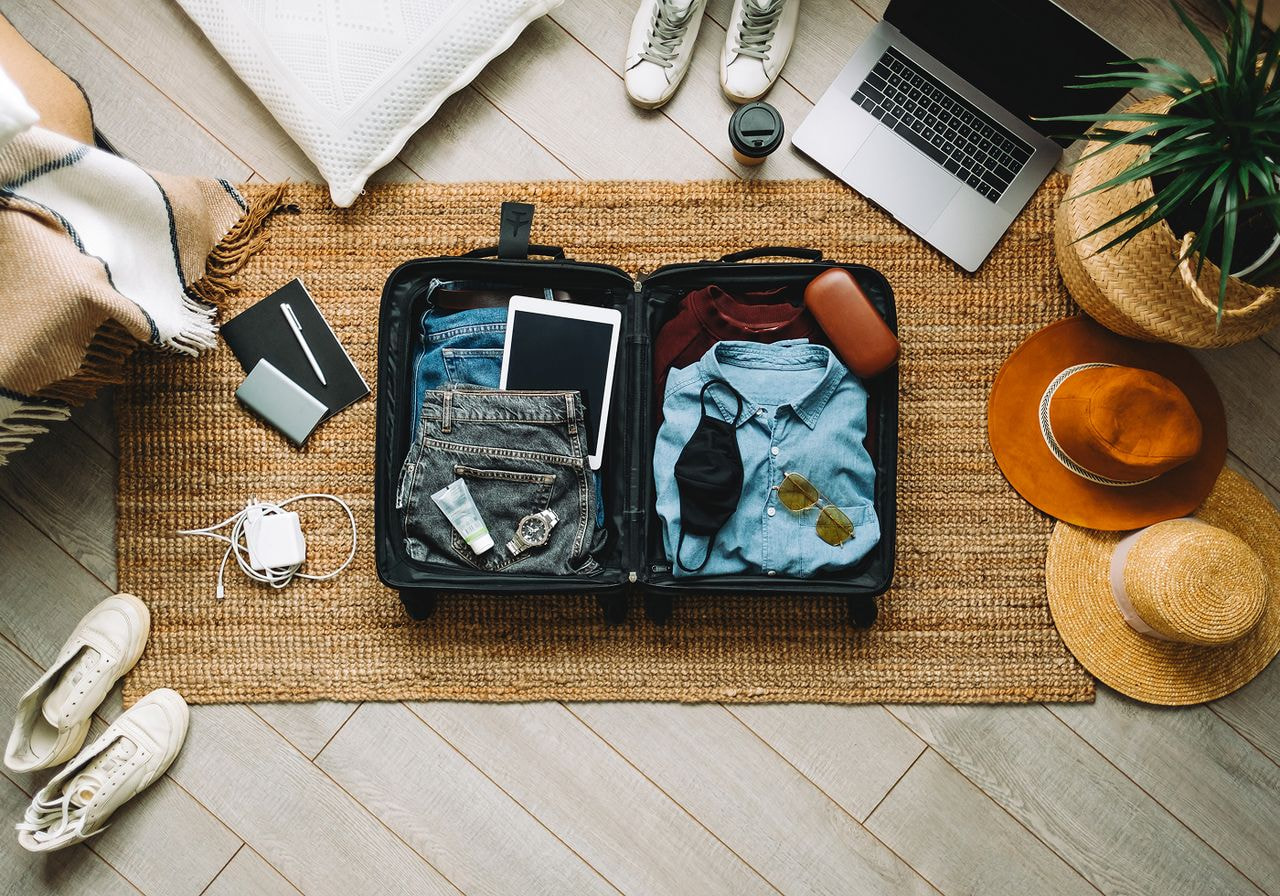 A suitcase filled with clothes and personal items placed on a patterned rug.