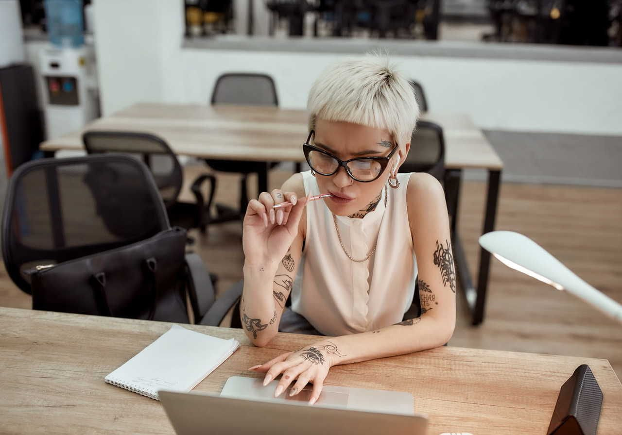A woman is sitting at a laptop, chewing on a pencil, thinking about how to create a custom calendar for 2026.