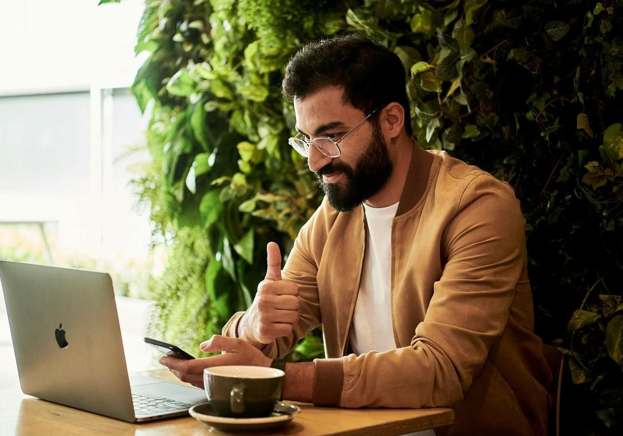 A man focused on a laptop while holding a smartphone in his other hand, engaged in multitasking.