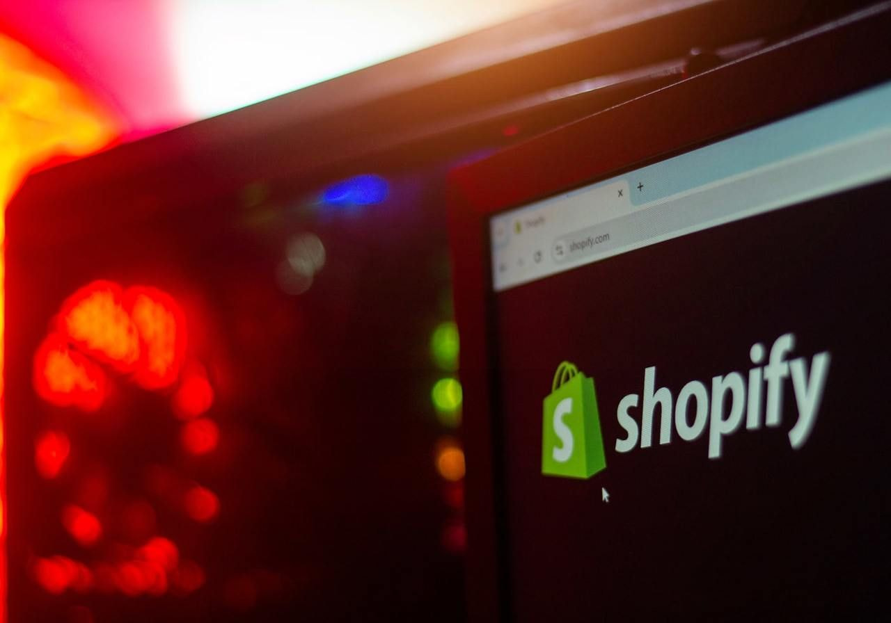 A close-up shot of Shopify’s logo on a corner of a monitor with a PC case in the background.