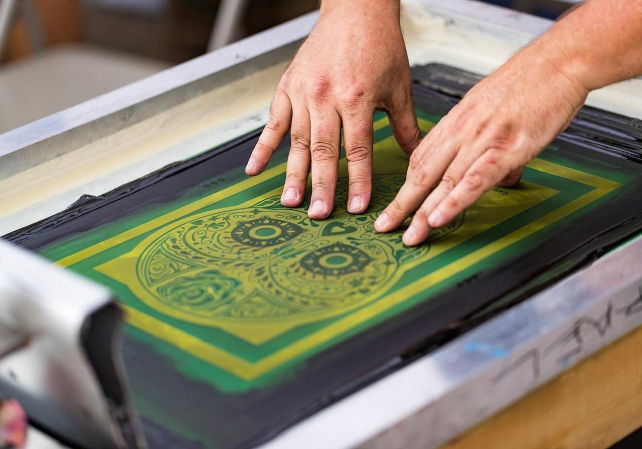 Hands carefully pressing a screen printing stencil with a green skull design.