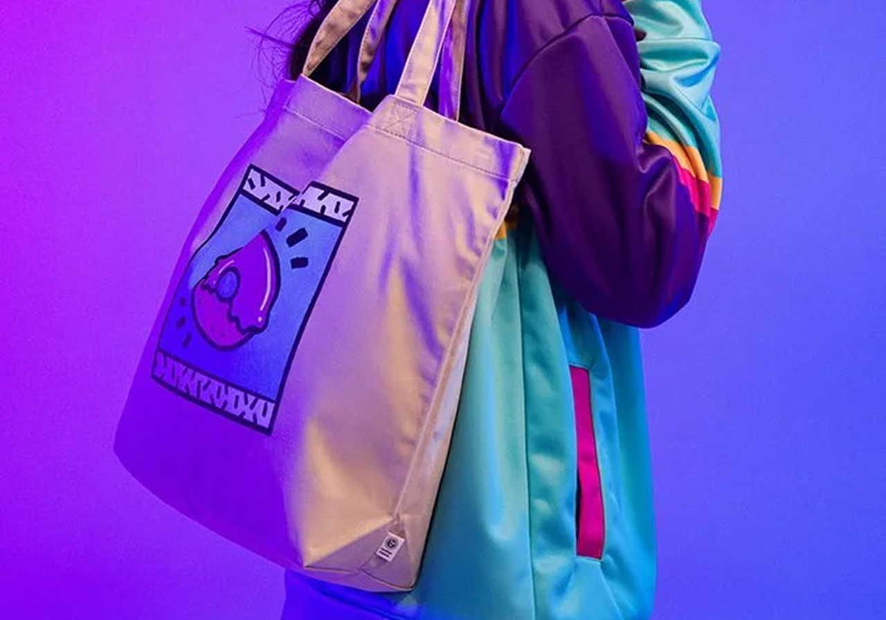 A person in a colorful track jacket holds a tote bag with a vibrant abstract design. The background is bathed in purple and blue light.