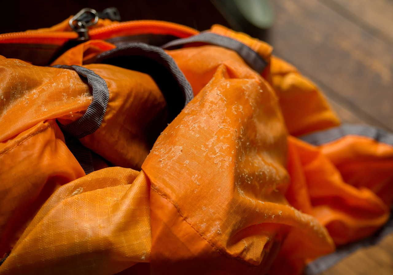 An orange waterproof backpack is partially unzipped, with visible water droplets on the fabric.