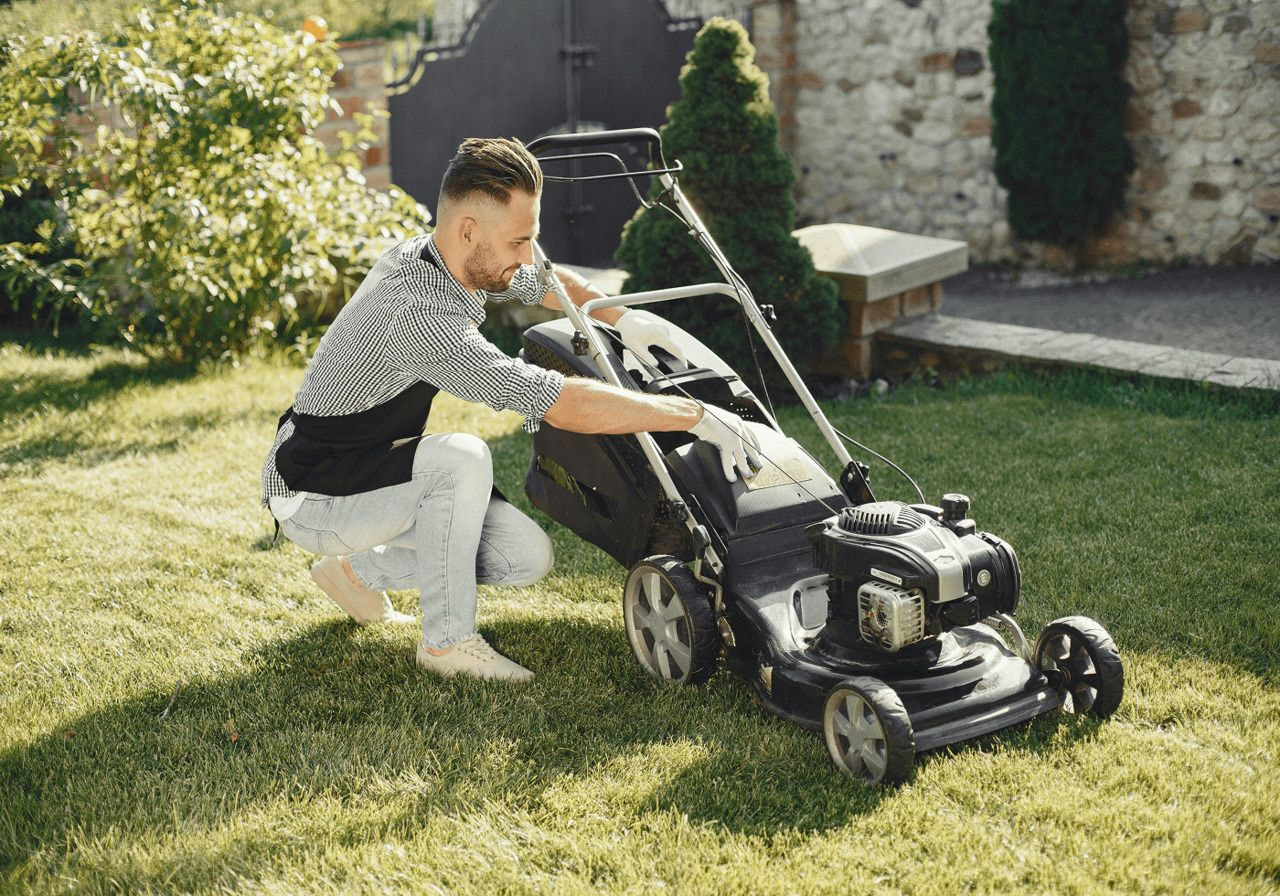 A man is using a lawn mower to cut grass in a well-maintained yard on a sunny day.