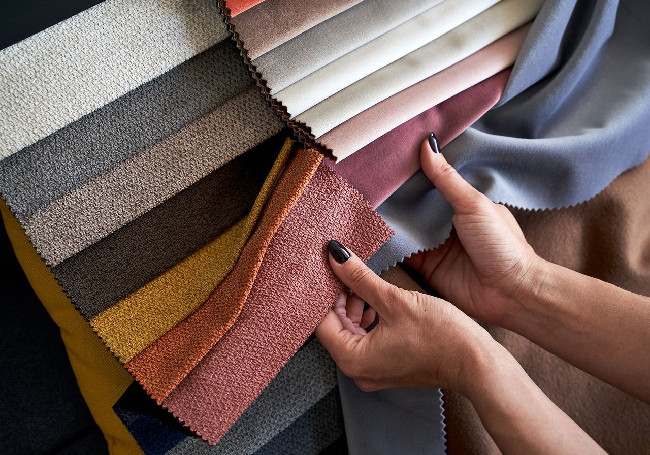 Hands sorting through a fanned-out selection of colorful textured fabric swatches.