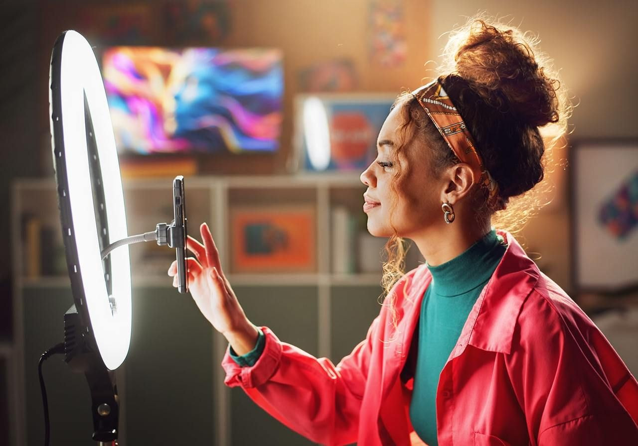 A young woman is filming herself with a mobile phone and using a lightstand.