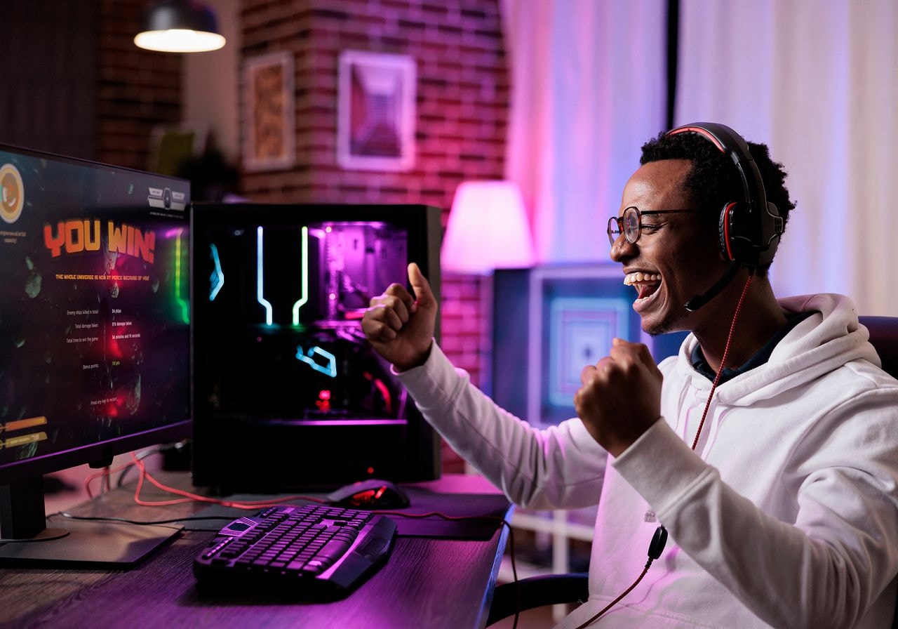 Man wearing a gaming headset celebrating a 'You Win' screen at his computer setup.