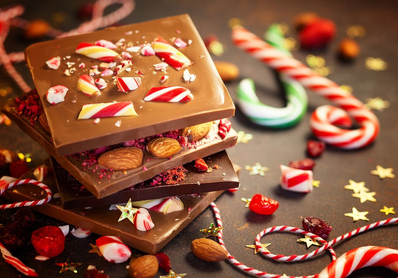 Stacked chocolate bark pieces topped with crushed candy canes, almonds, and dried berries, surrounded by candy canes and gold star confetti.