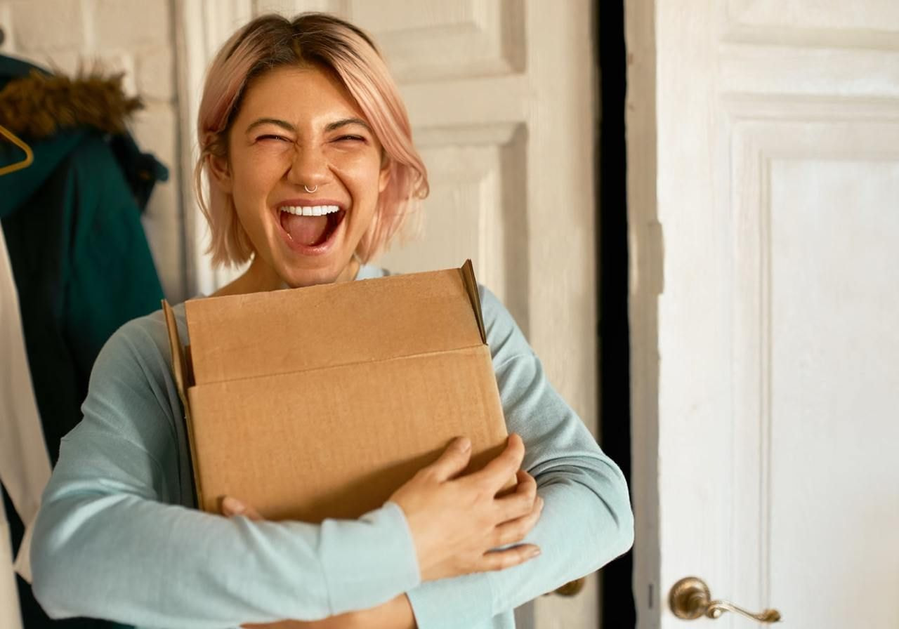 A woman laughs while holding a cardboard box, conveying joy and excitement in a lighthearted moment.