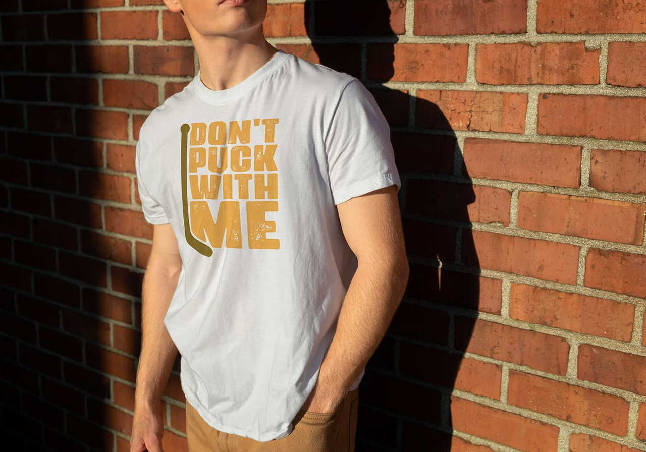 A person wearing a white t-shirt with the words "DON'T PUCK WITH ME" stands against a sunlit brick wall, casting a shadow.