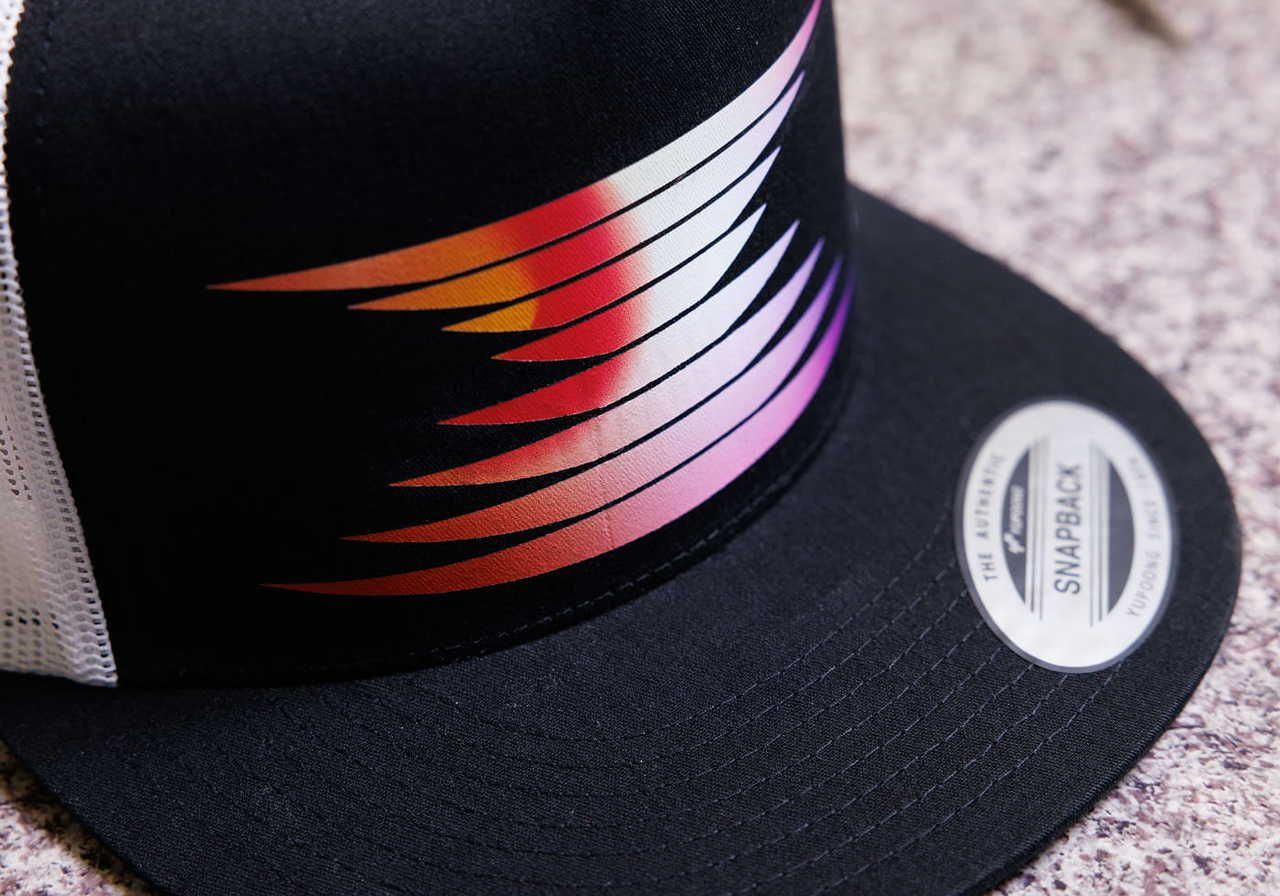 A close-up of a black snapback hat with a colorful, abstract striped design on the front.