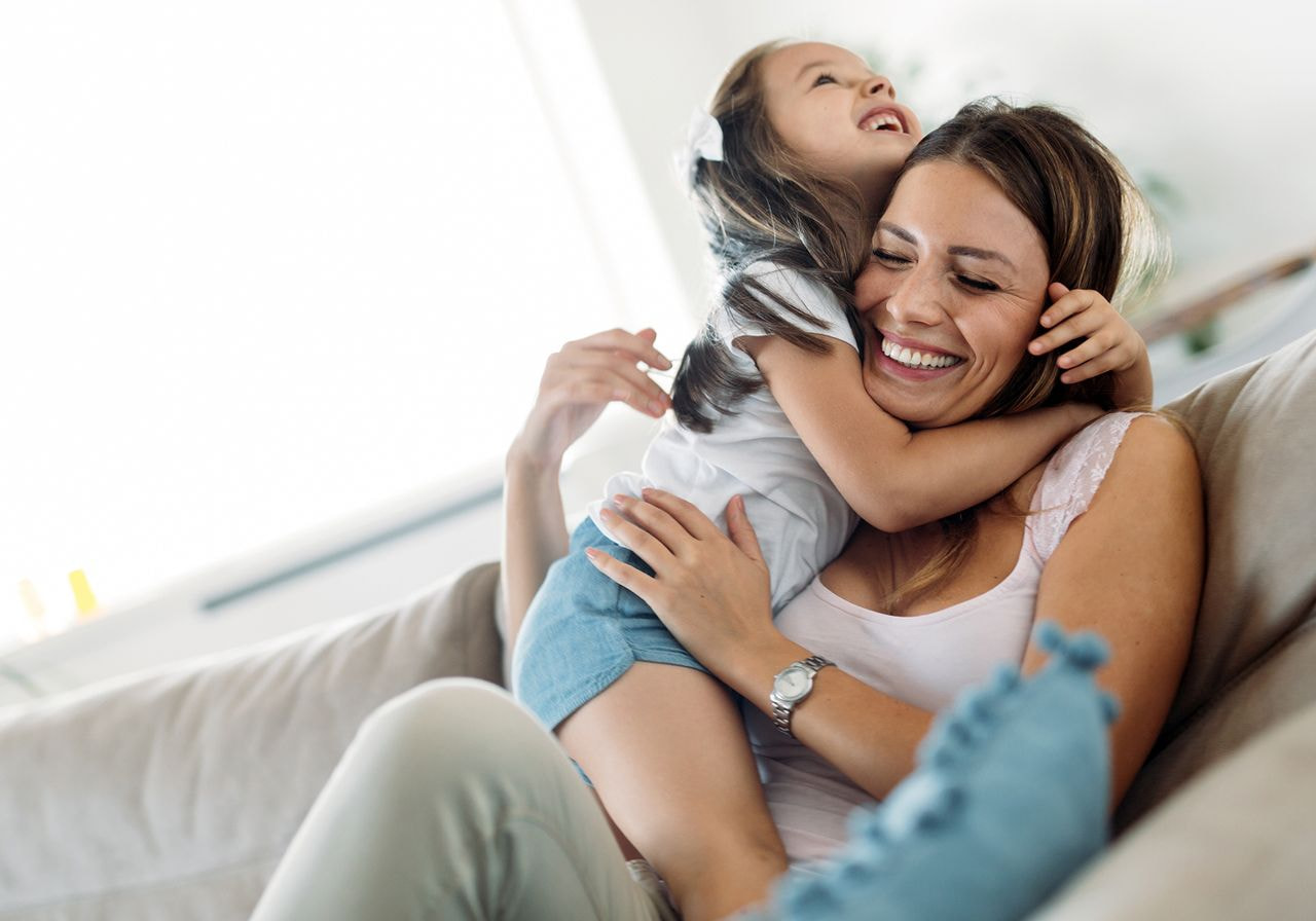 A woman and her daughter sit together on a couch, sharing a moment of relaxation and connection.