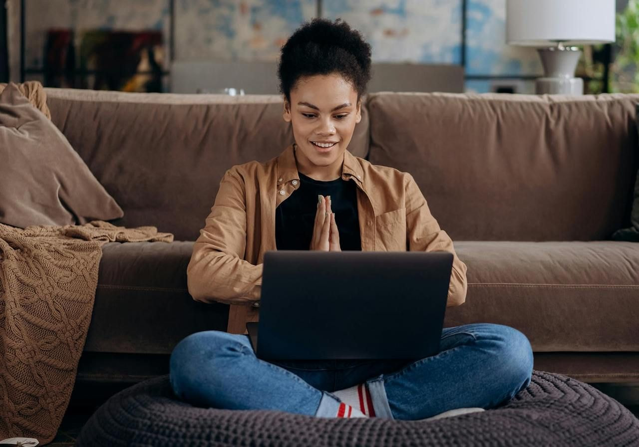 A woman is sitting on a floor pillow with a laptop and is looking at the screen.