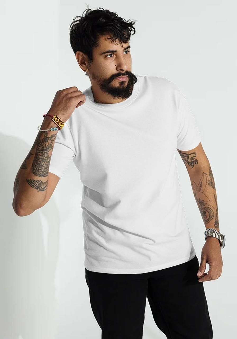 A man with a beard wearing a white t-shirt and black pants, showcasing colorful bracelets and tattoos.