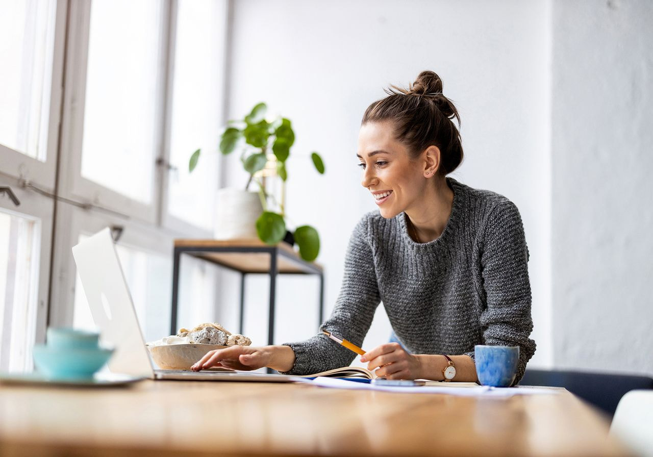 Woman smiling while working at a laptop in a bright room.