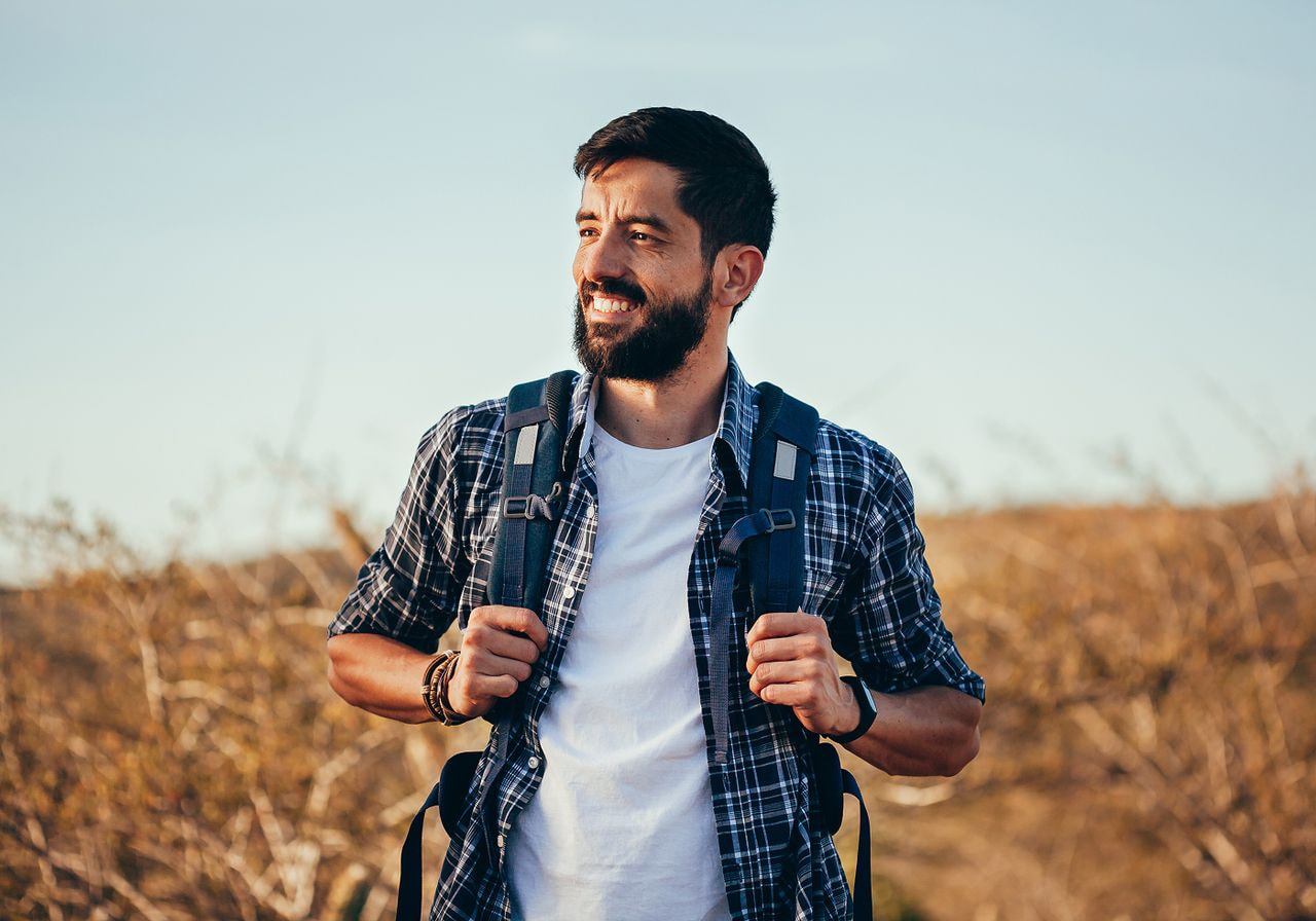A smiling man with a beard wearing a backpack, exuding a friendly and approachable demeanor.