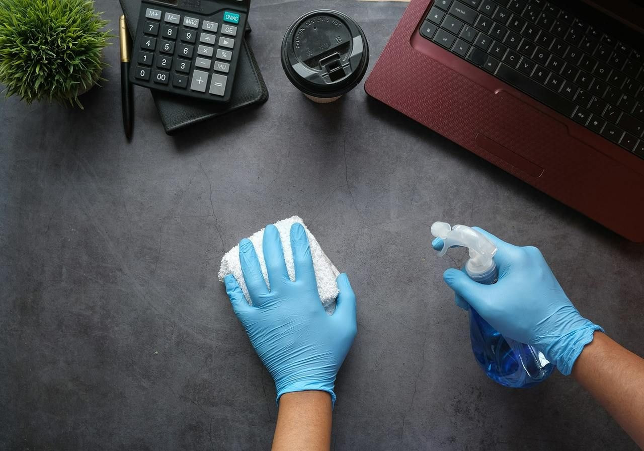 A person in blue gloves cleans a laptop with a blue rubber glove, focusing on maintaining device hygiene.