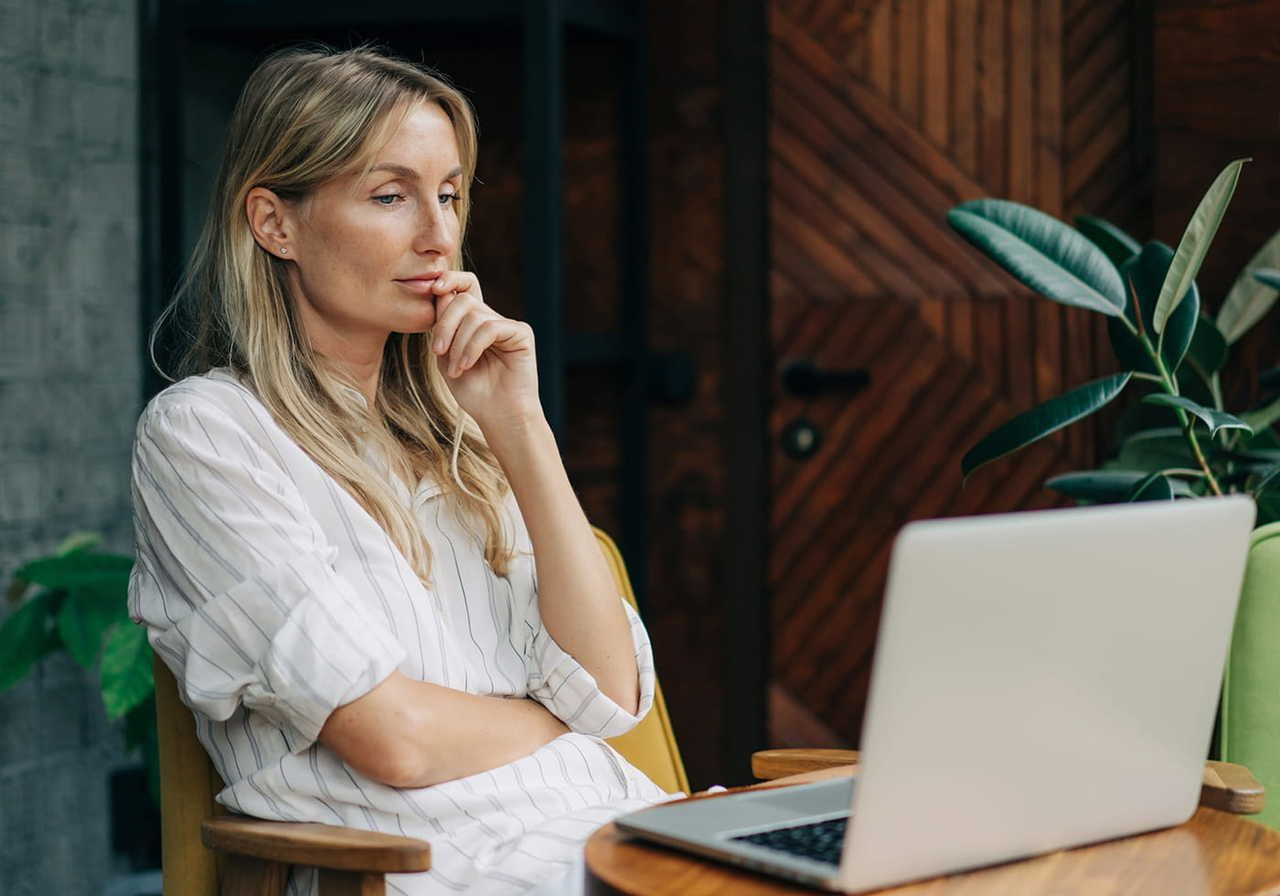 A woman is looking at a laptop while sitting in a cafe, browsing to learn how to make money from home