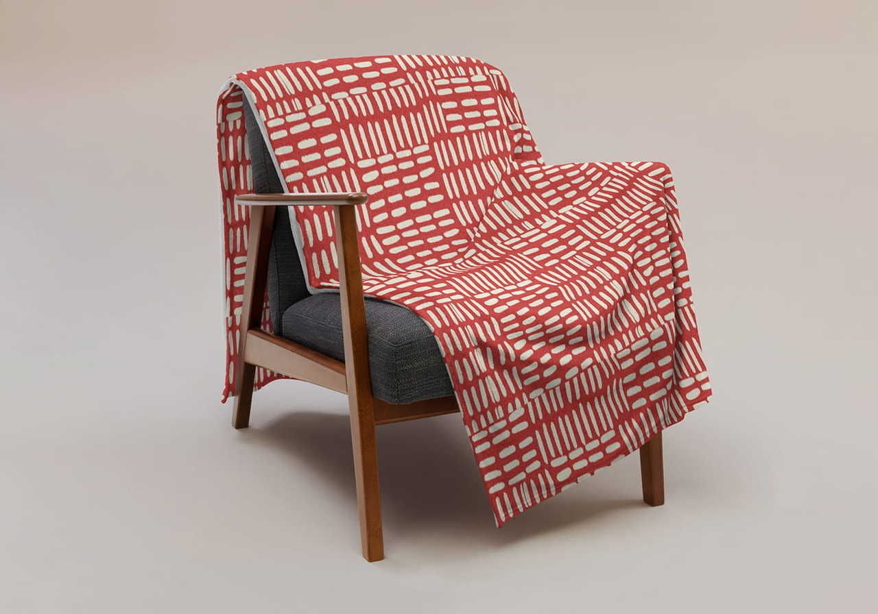 A wooden armchair with a gray cushion is draped with a red and white geometric-patterned blanket.