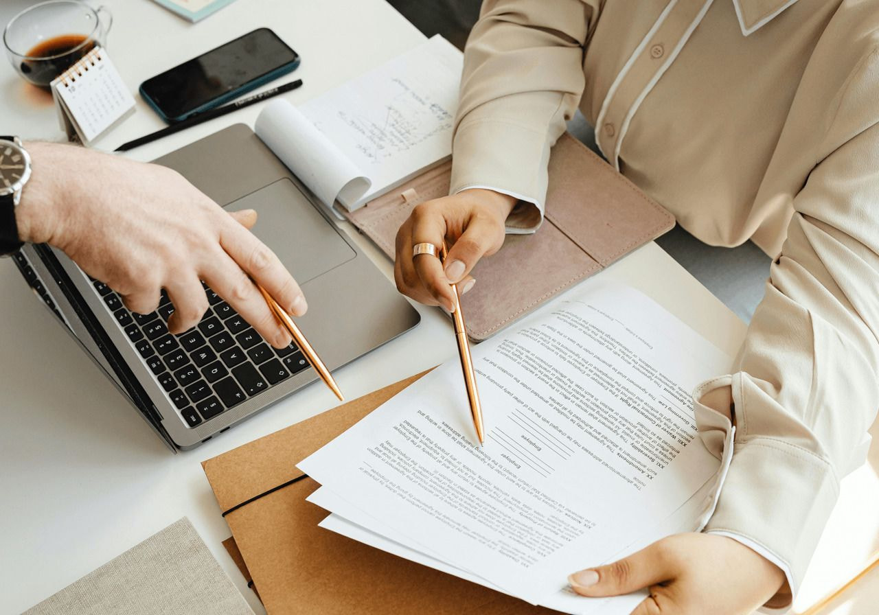 Two individuals collaborating on paperwork at a desk, focused on their tasks in a professional setting.