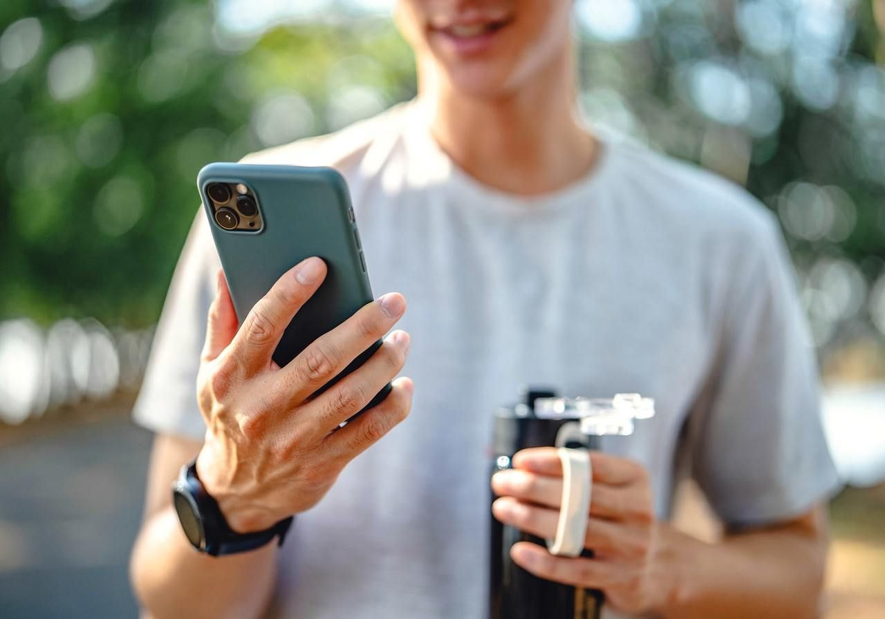 A man is holding a mobile phone in one hand and a water bottle in the other. 