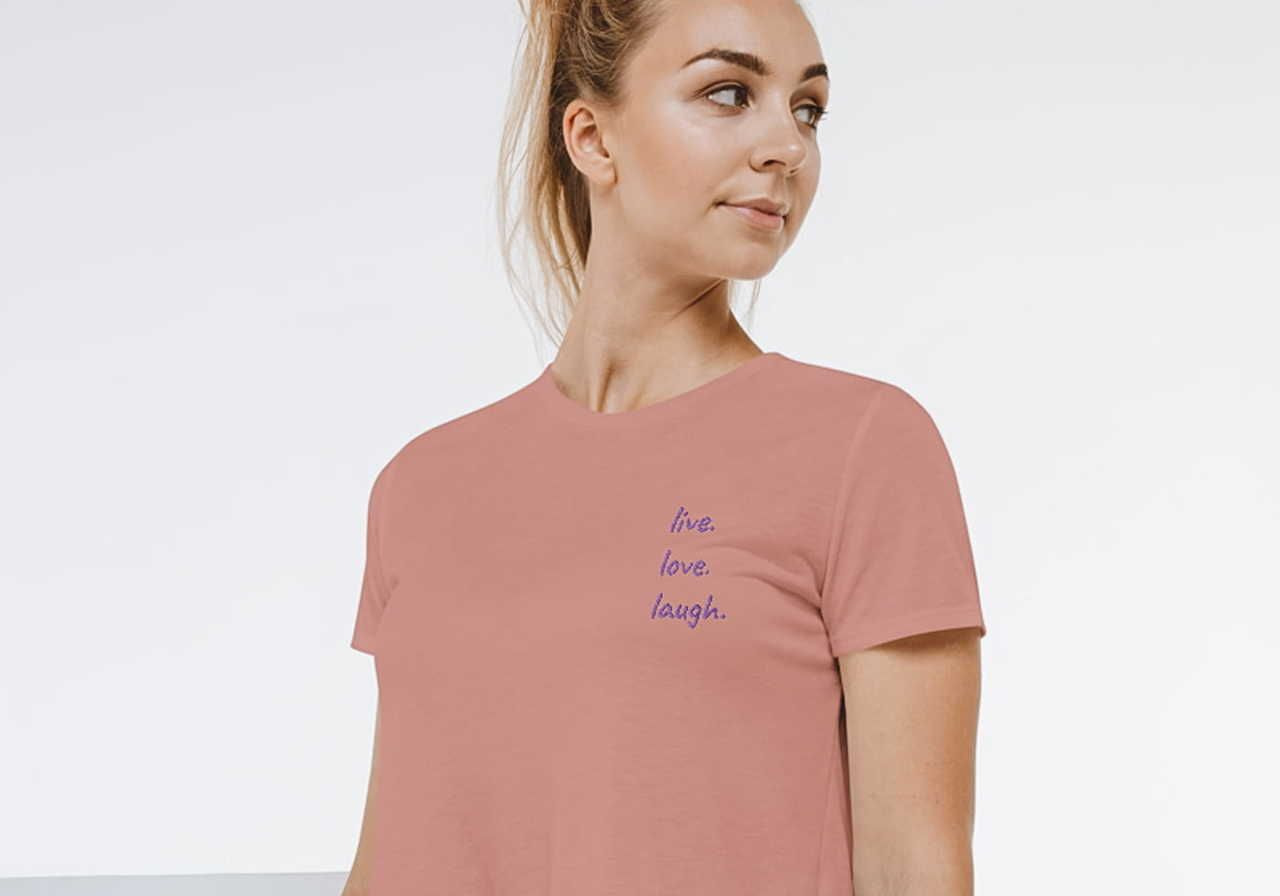A woman wearing a pink t-shirt with the phrases "live," "love," and "laugh" printed on it.