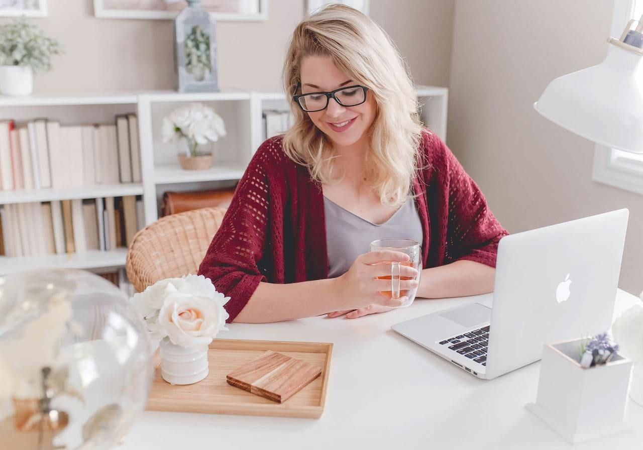 A woman sitting at a desk, working on a laptop with a glass of water beside her.