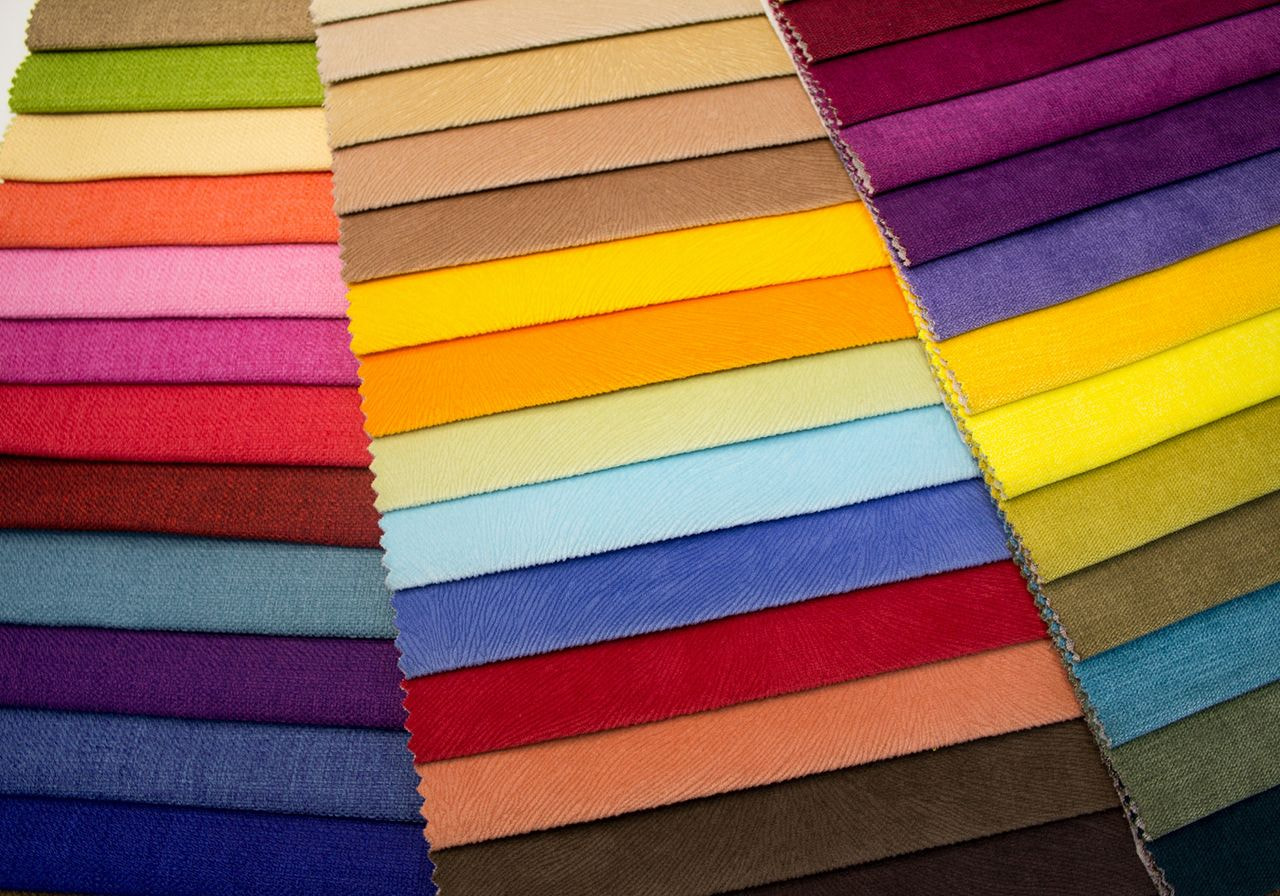 A vibrant display of fabric swatches in various colors, including reds, yellows, blues, and greens, arranged in neat horizontal rows, evoking a sense of creativity.