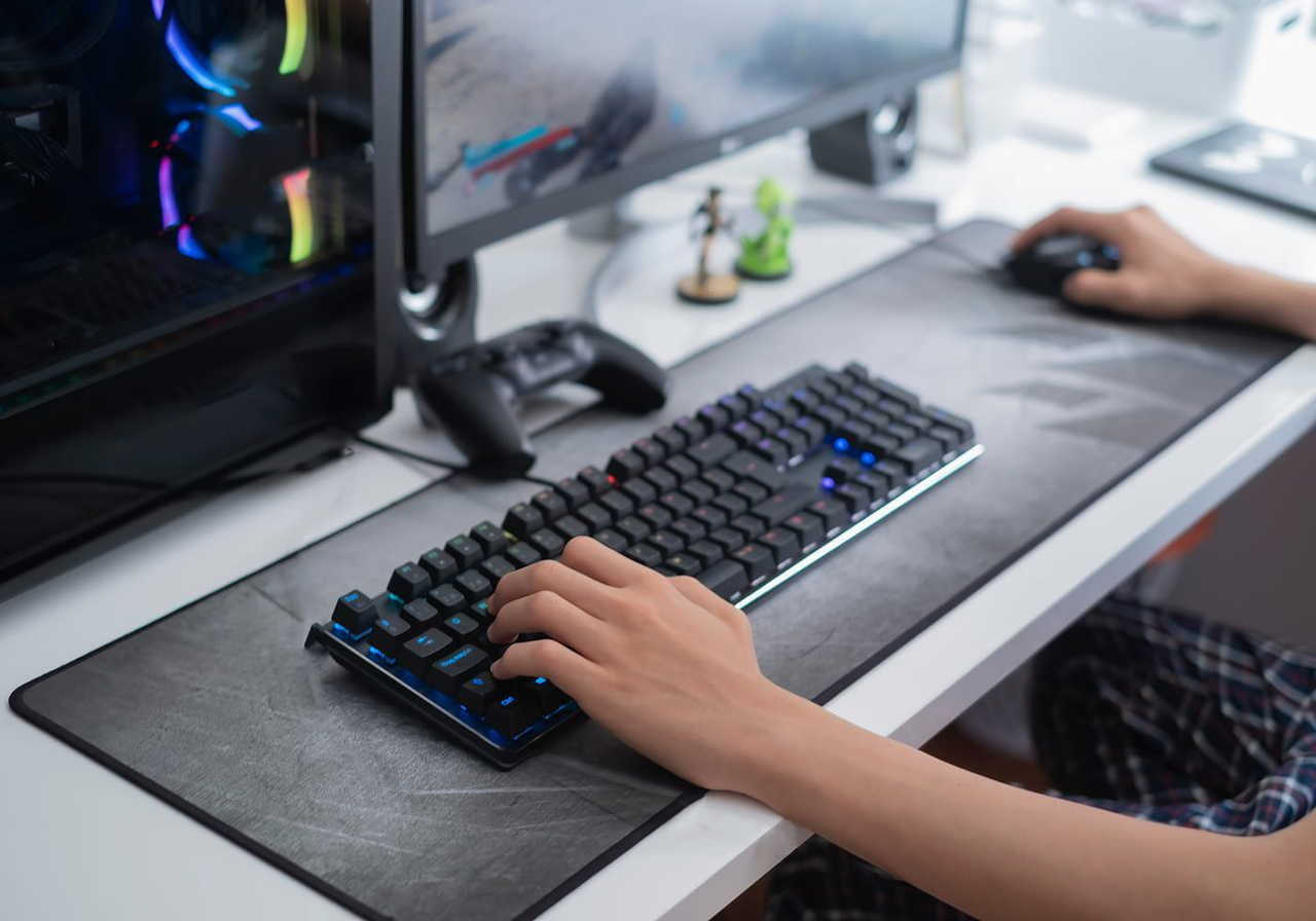 A person is playing on a PC. Monitor, keyboard, desktop mat, and the PC are visible.