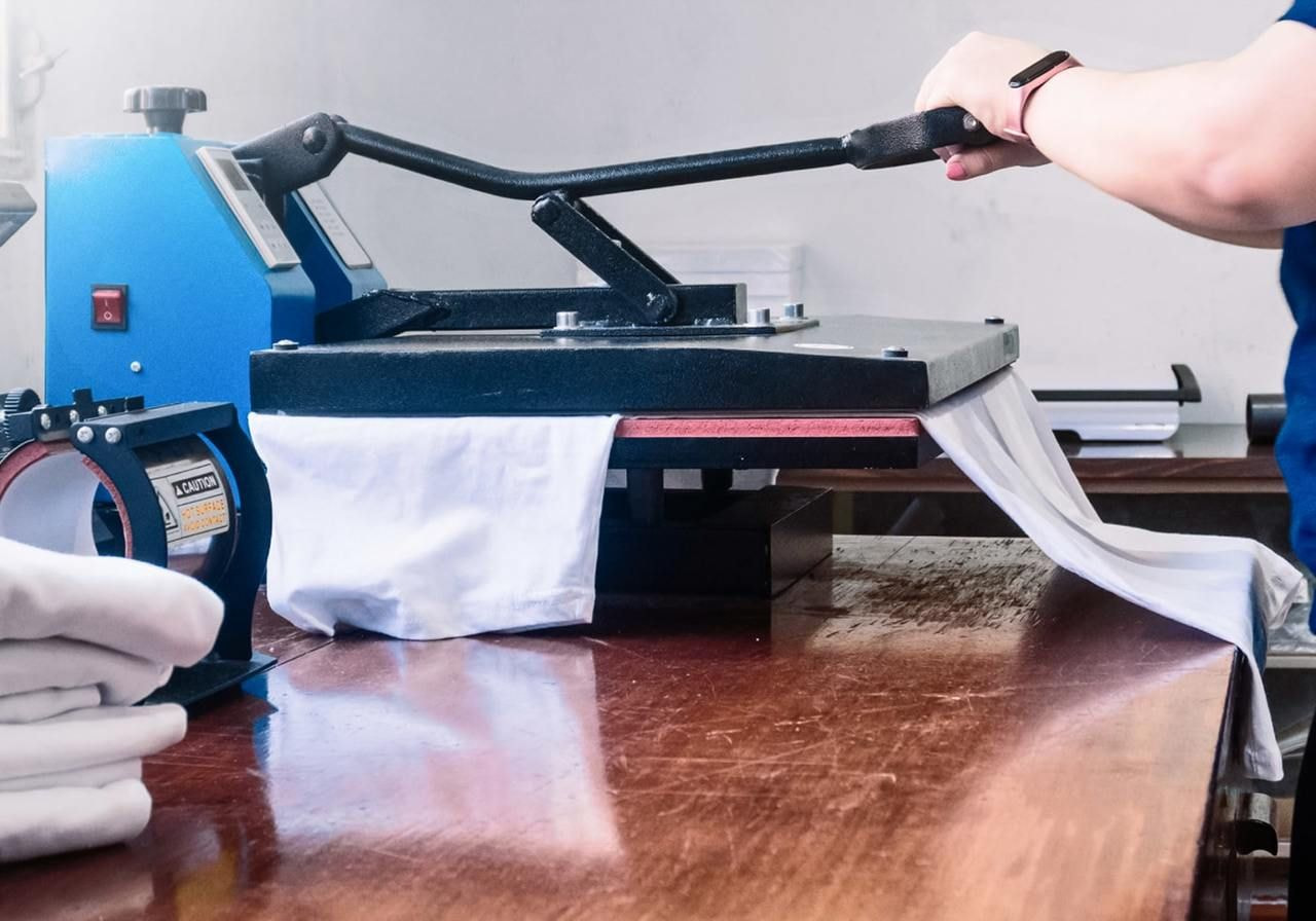 A person operates a machine to produce shirts in a workshop setting, focused on their task.