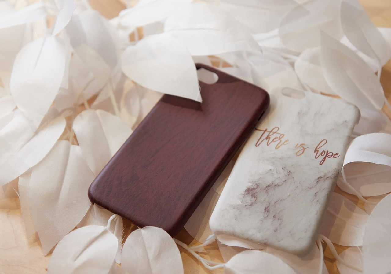 Two phone cases resting on a bed of white leaves; one is brown, and the other is marble-patterned with the text "this is hope”.
