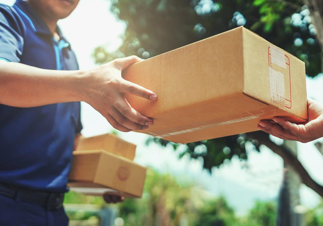 A man hands a package to another person in a casual exchange outdoors.