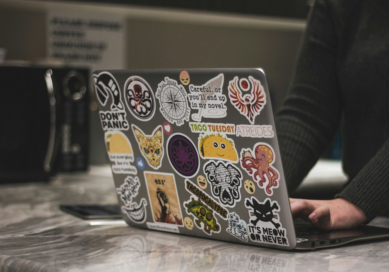 A person sitting at a desk, working on a laptop adorned with various colorful stickers.