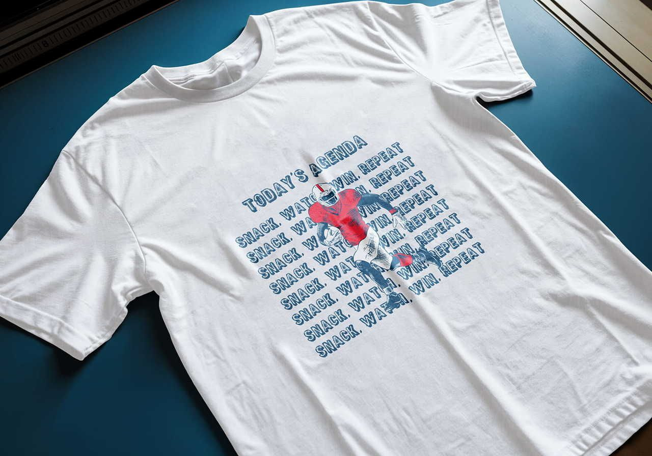 White t-shirt featuring a graphic of a football player in red and blue with the text "Today's Agenda: Snack, Watch, Win, Repeat" in bold letters.