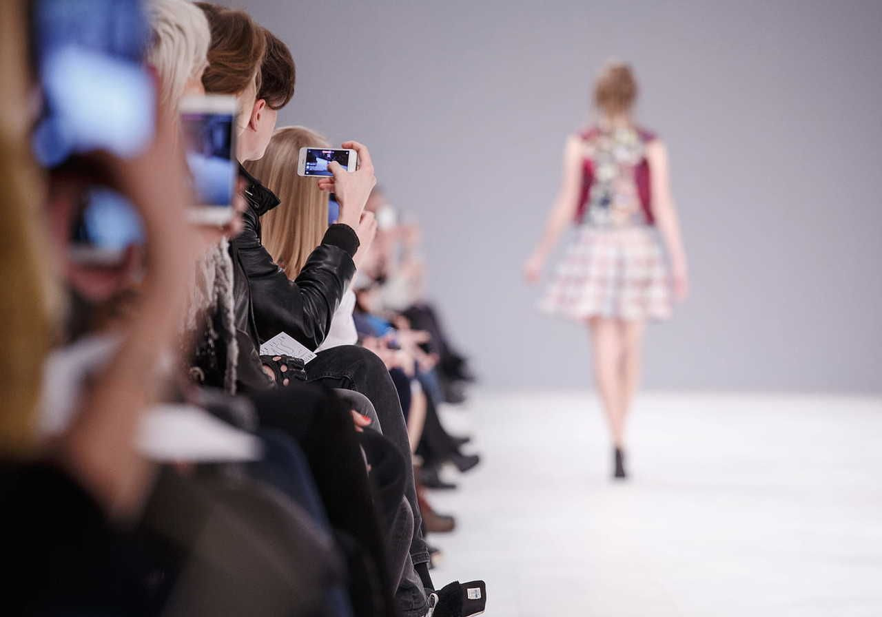 Focus set on a group of people taking pictures of a model during a fashion show.