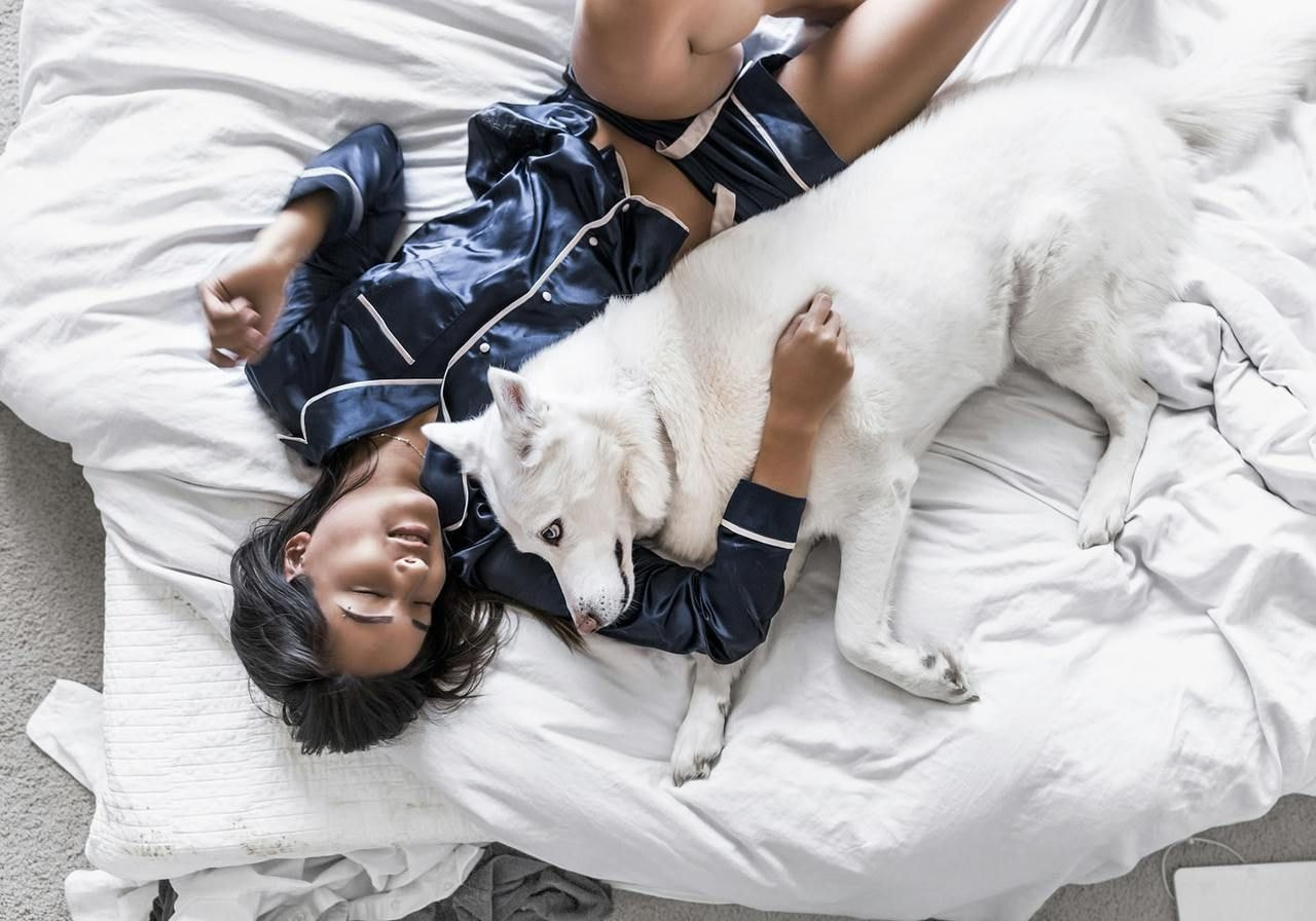A woman reclines on a bed, gently resting beside a fluffy white dog.