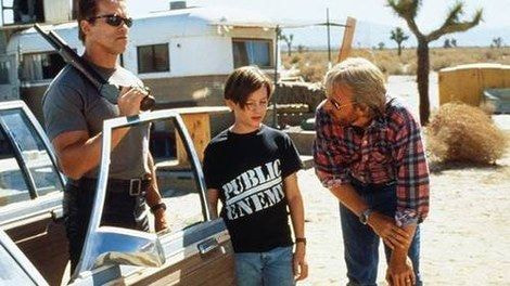 A kid in a t-shirt with a couple of a grown adults next to a car.
