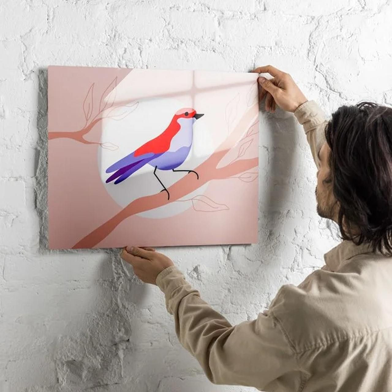 A man is hanging a metal print of an illustrated bird.