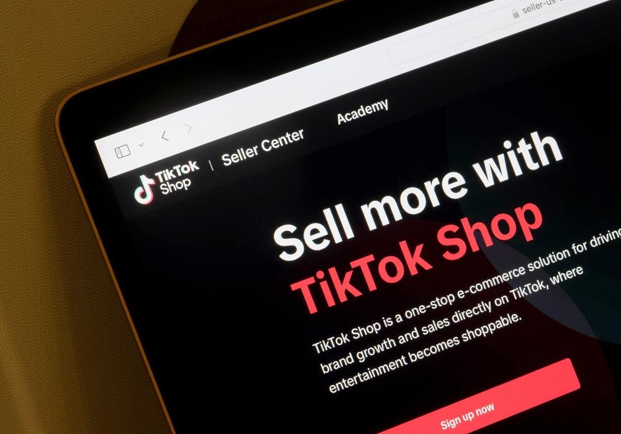 Close-up of a tablet screen displaying the TikTok Shop website with the text "Sell more with TikTok Shop" on a dark background.