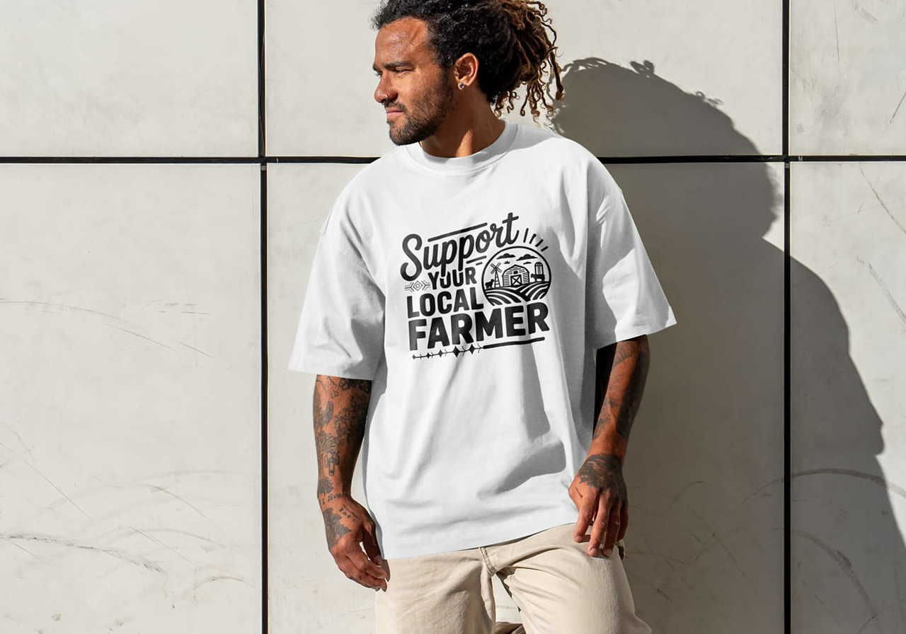 Man with dreadlocks wearing a white t-shirt that reads "Support Your Local Farmer" in bold letters, standing against a tiled wall.