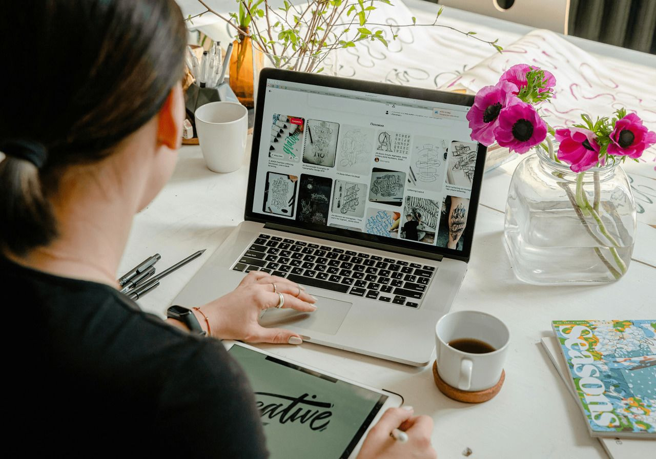 A woman focused on her laptop, working diligently at a tidy desk with a notepad and a plant nearby.
