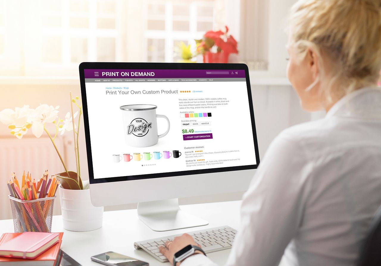 A woman sits at a desk, focused on her computer screen, with a notepad and pen beside her.