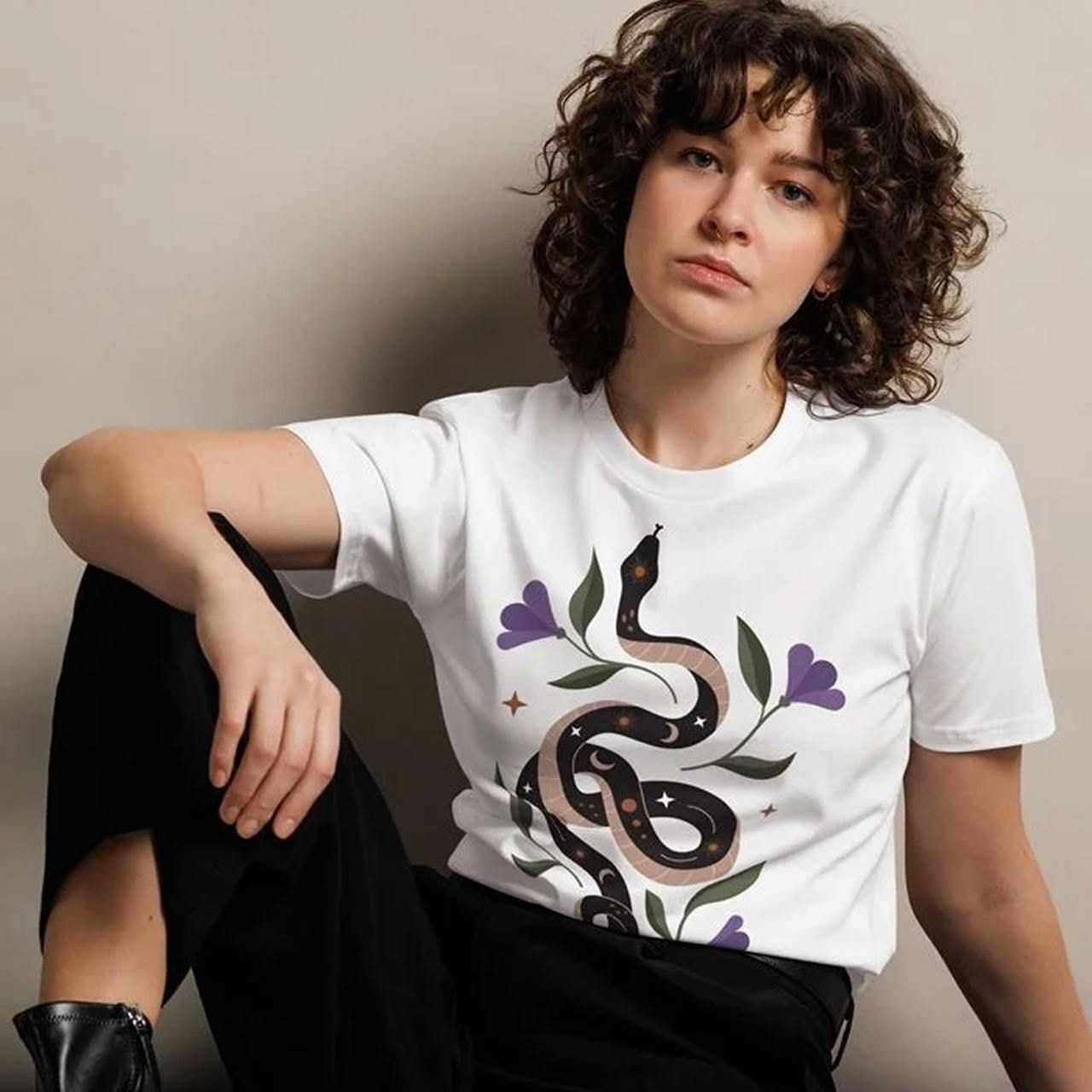 A woman with curly hair wearing a white t-shirt made with DTG printing featuring a snake design with leafy accents.